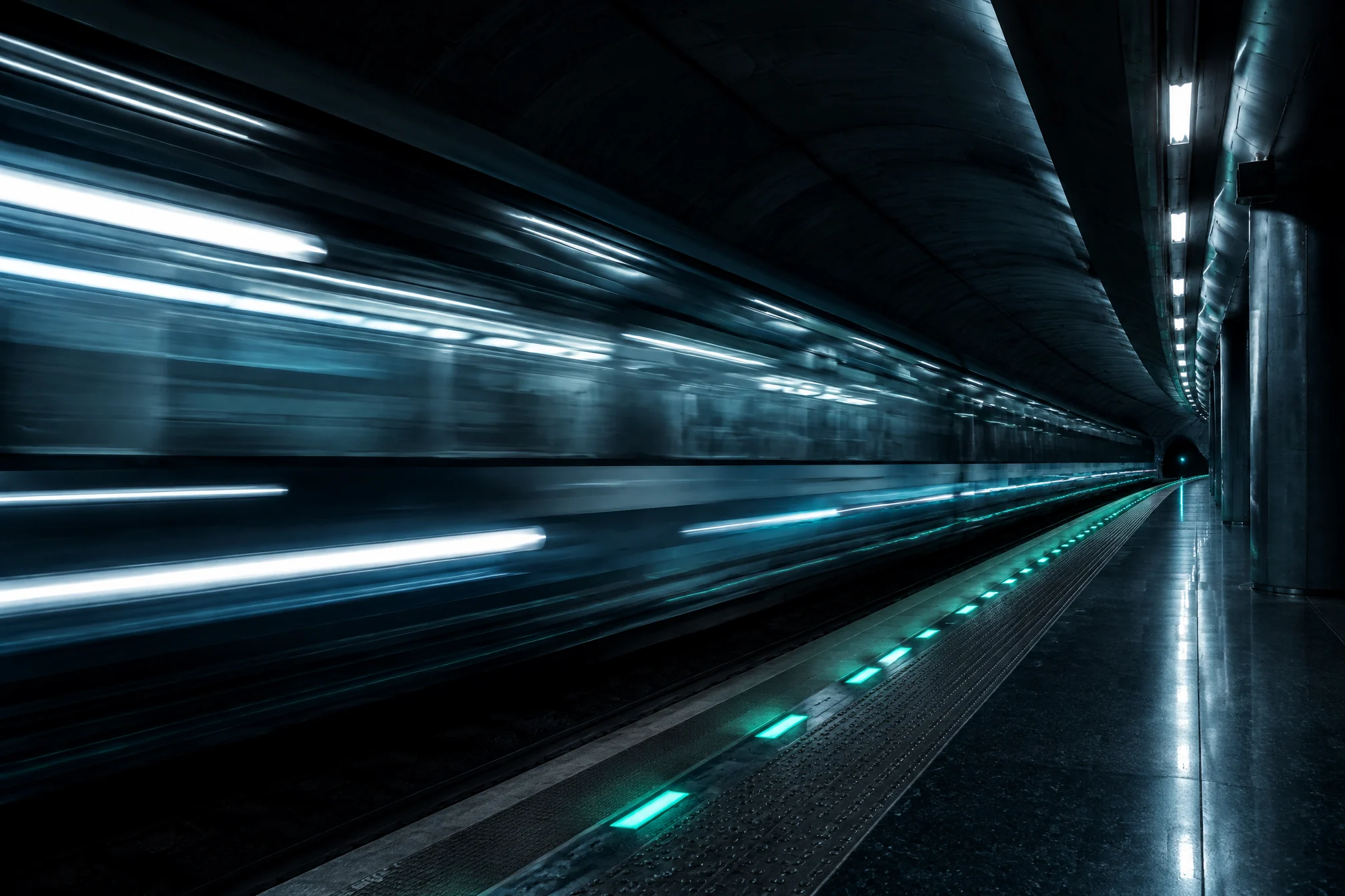 Metro train streaking through a dark station past mint platform lights
